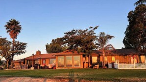 A two-story wooden house with large windows, a fenced yard, and a palm tree. - FarmStay HillTop wine country views 6BR/4BA (Paso Robles)