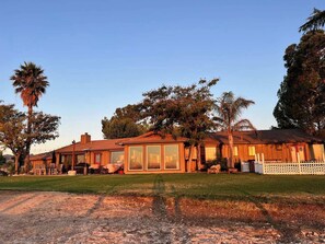 A two-story wooden house with large windows, a fenced yard, and a palm tree.
