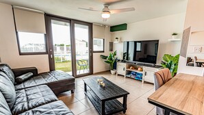 A modern living room with a leather sofa, a wooden coffee table, a TV, and a dining area with a wooden table and chairs. - 3 Bedroom Oceanfront Beach House (Isabela)