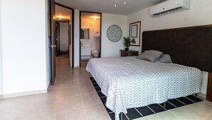 A bedroom with a bed, a ceiling fan, an air conditioning unit, a bathroom visible through an open door, and a tiled floor. - 3 Bedroom Oceanfront Beach House (Isabela)