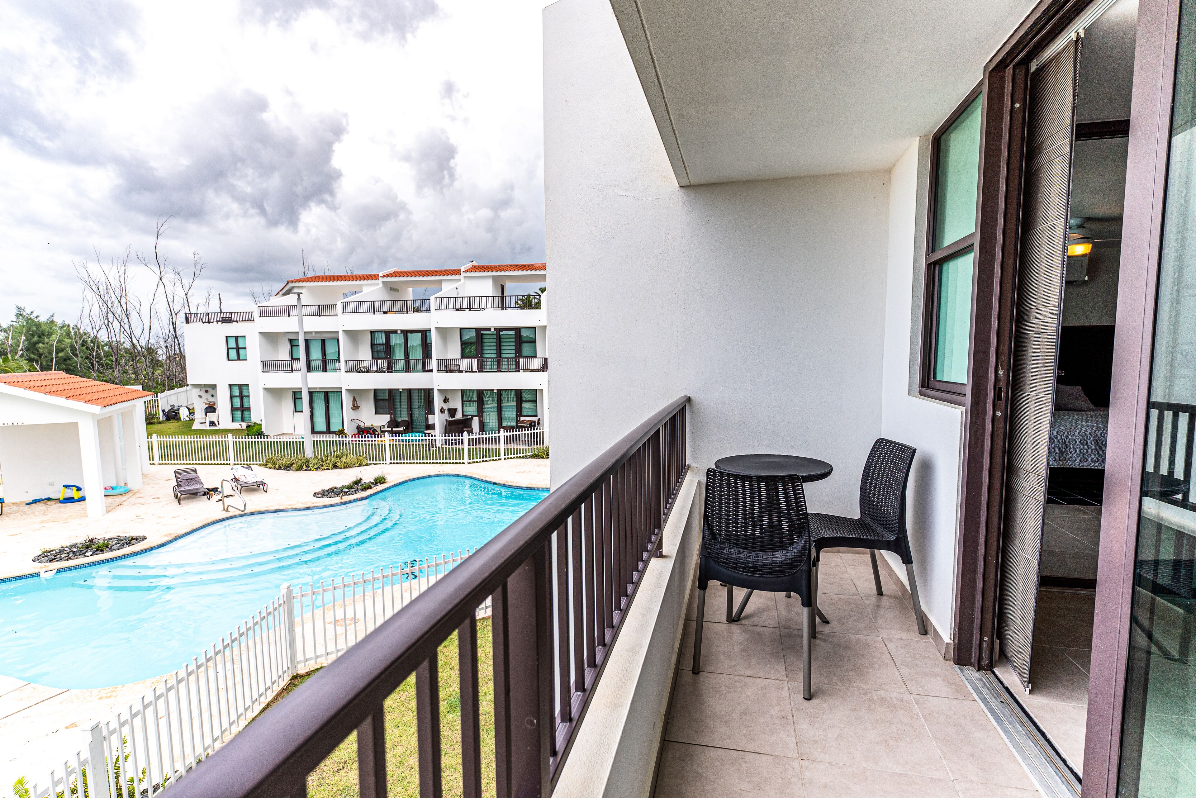 A balcony with a view of a swimming pool and a building with multiple balconies.
