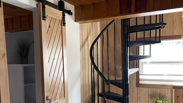 Un intérieur en bois agrémenté d’un escalier en colimaçon, d’une porte coulissante de style grange et d’une petite plante en pot.