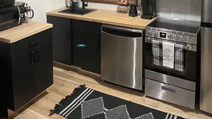 Une cuisine moderne avec des meubles de couleur noire, un plan de travail en bois, une cuisinière en acier inoxydable et un lave-vaisselle.