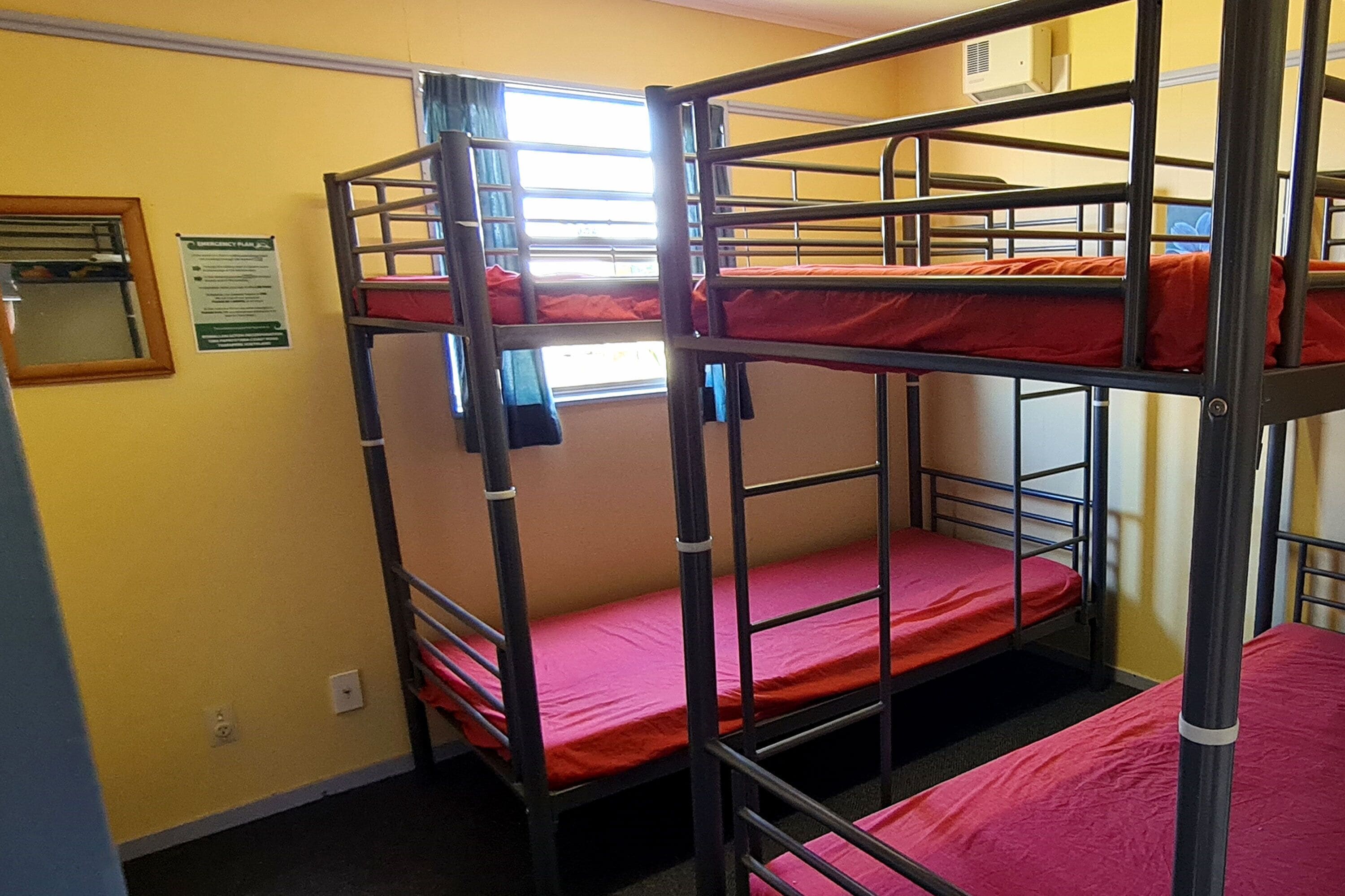 A bunk bed room with yellow walls, a window with curtains, and a mirror on the left wall.
