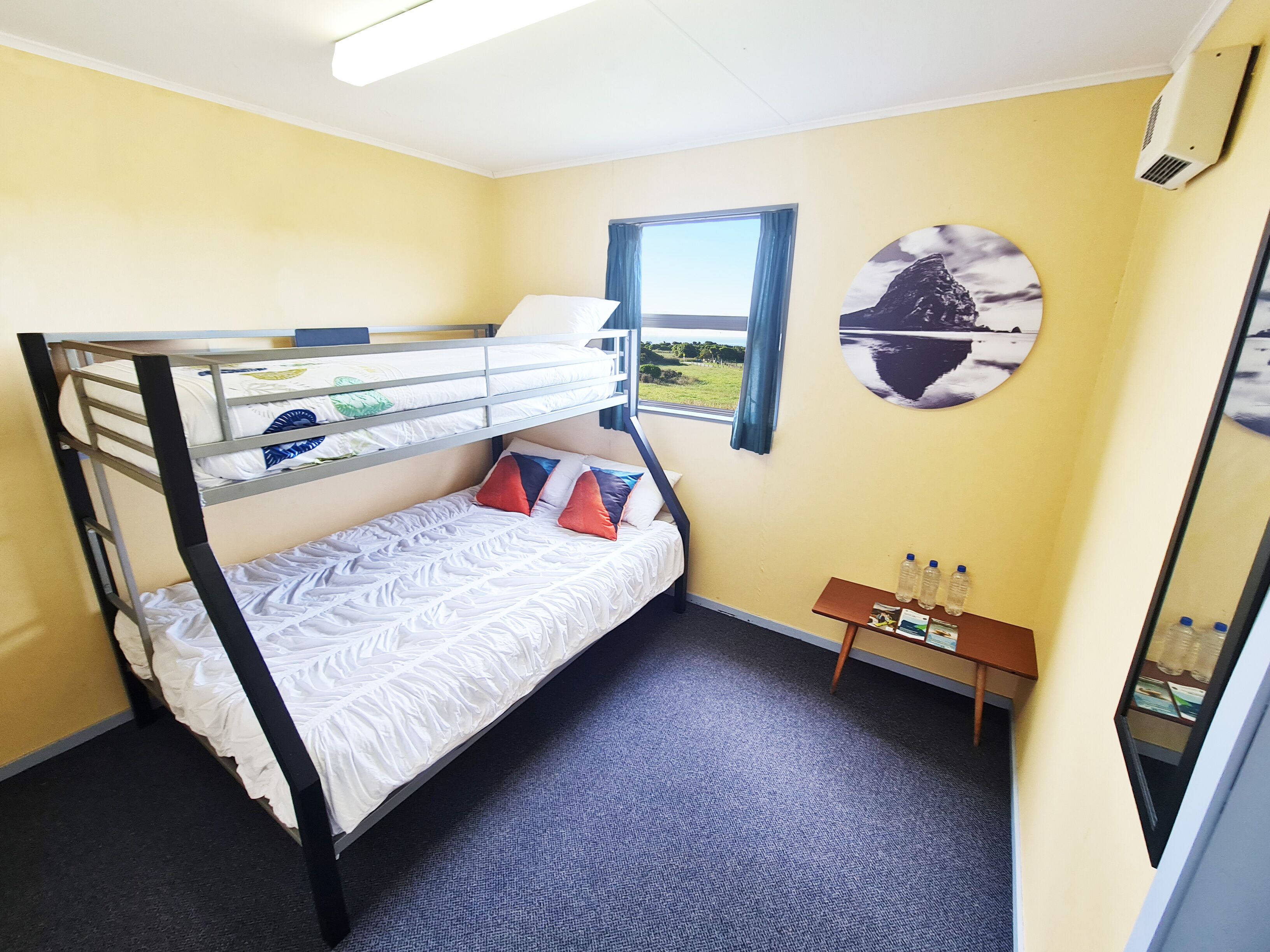 A bunk bed room with a window, a small table with water bottles, and a circular wall decoration.