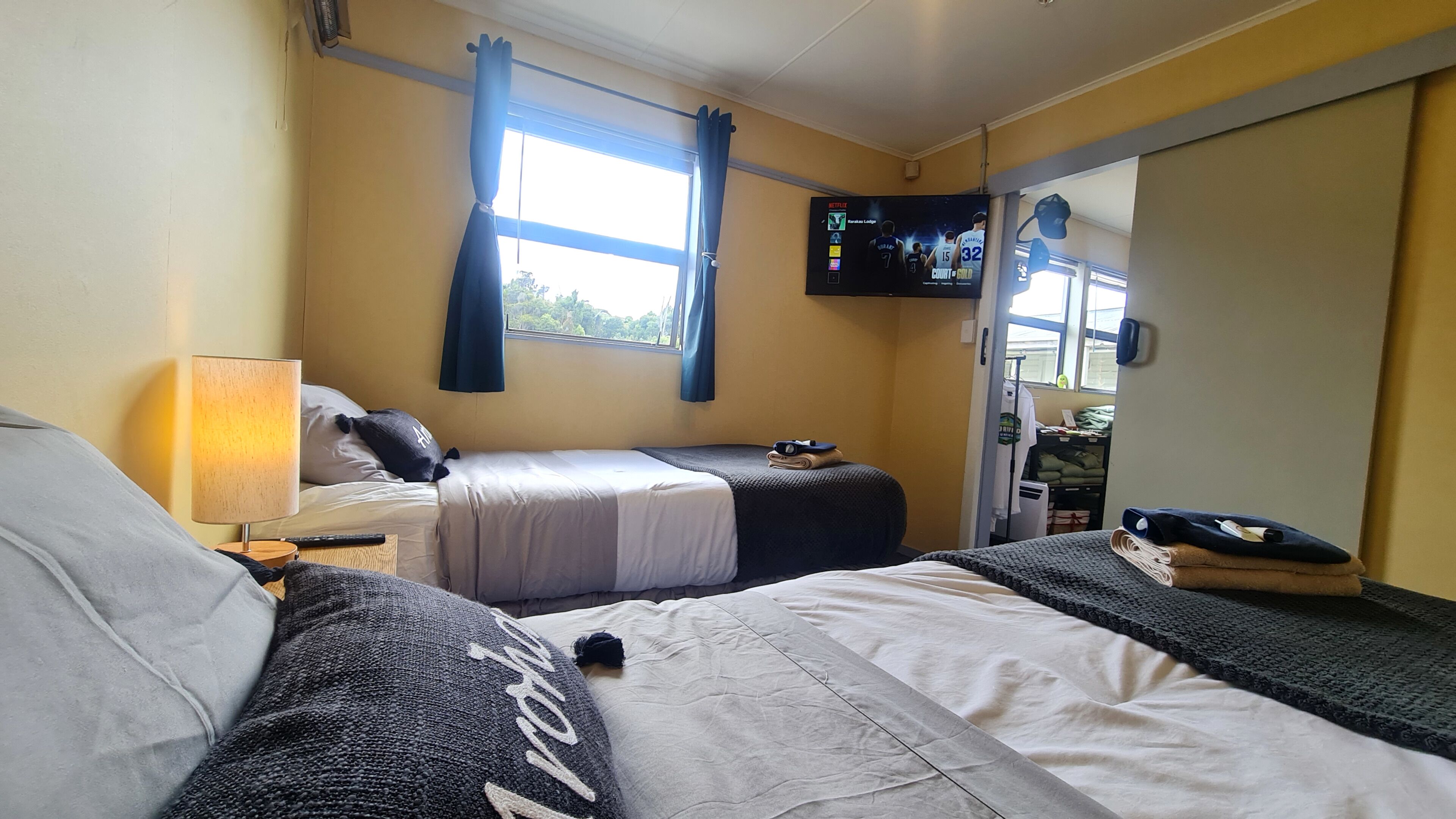 A hotel room with two beds, a TV mounted on the wall, and a window with curtains.