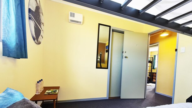 A hotel room with a bed, a desk, a mirror, and a door leading to another room. - Rarakau Lodge (Rowallan)
