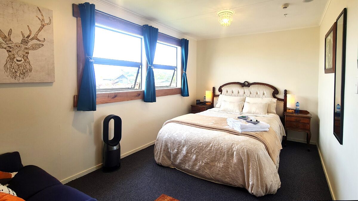A bedroom with a bed, a bedside table, a lamp, a heater, and a window with curtains.