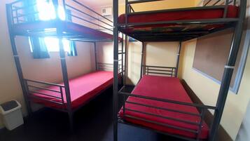 A dormitory room with bunk beds, a small trash bin, and a window.
