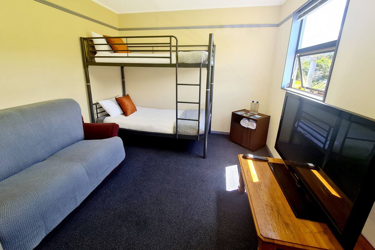 A bunk bed with a TV, a sofa, and a small table with a remote control.