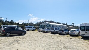 A parking area with several vehicles, including vans and cars, and a building with a sign that reads "RARAKAU". - Rarakau Lodge (Rowallan)