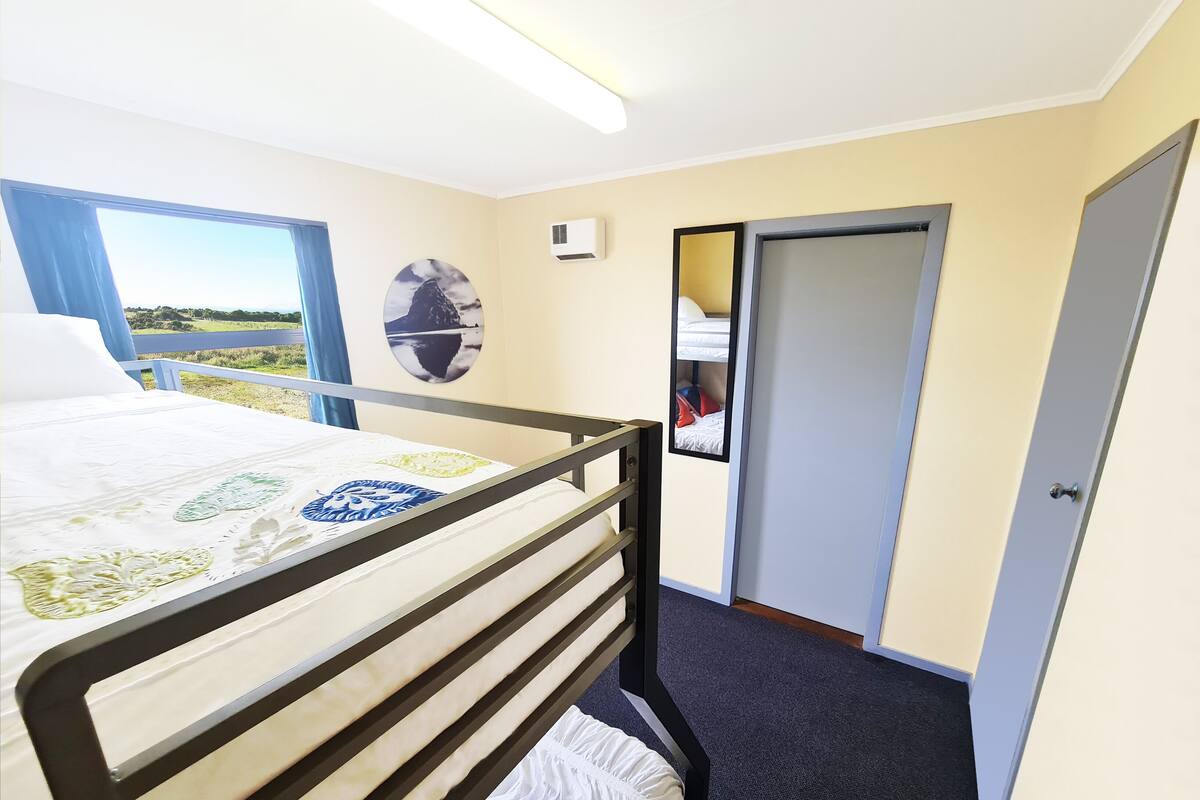 A bedroom with a bed, a window with a view, a door, and a wall-mounted air conditioner.