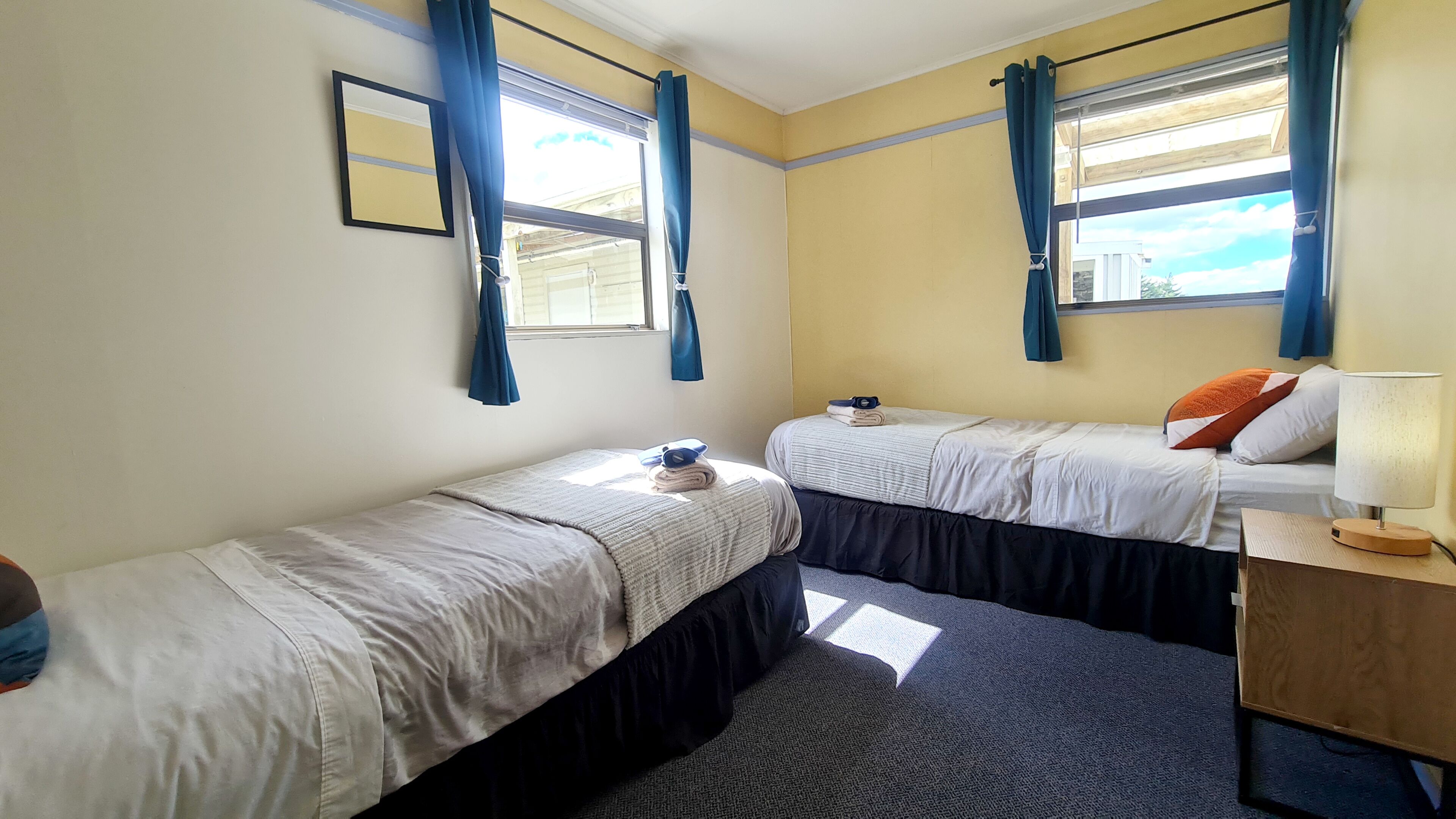 Quarto com duas camas, mesa de cabeceira com abajur e janela com cortinas.