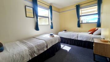 Quarto com duas camas, mesa de cabeceira com abajur e janela com cortinas.