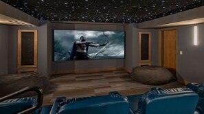 Ein Heimkino mit einem großen Flachbildfernseher, Holzböden und blauen Sitzmöglichkeiten.