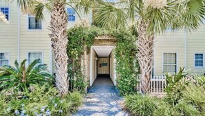 A pathway leading to a building with a covered entrance, surrounded by lush greenery and palm trees. - 30A Gulf front 2 Bed/2 Bath Sleeps 6 Private beach- Beach service included (Santa Rosa Beach)