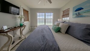 A bedroom with a bed, a desk with a computer, a TV, a window with blinds, and a painting of a beach scene. - 30A Gulf front 2 Bed/2 Bath Sleeps 6 Private beach- Beach service included (Santa Rosa Beach)