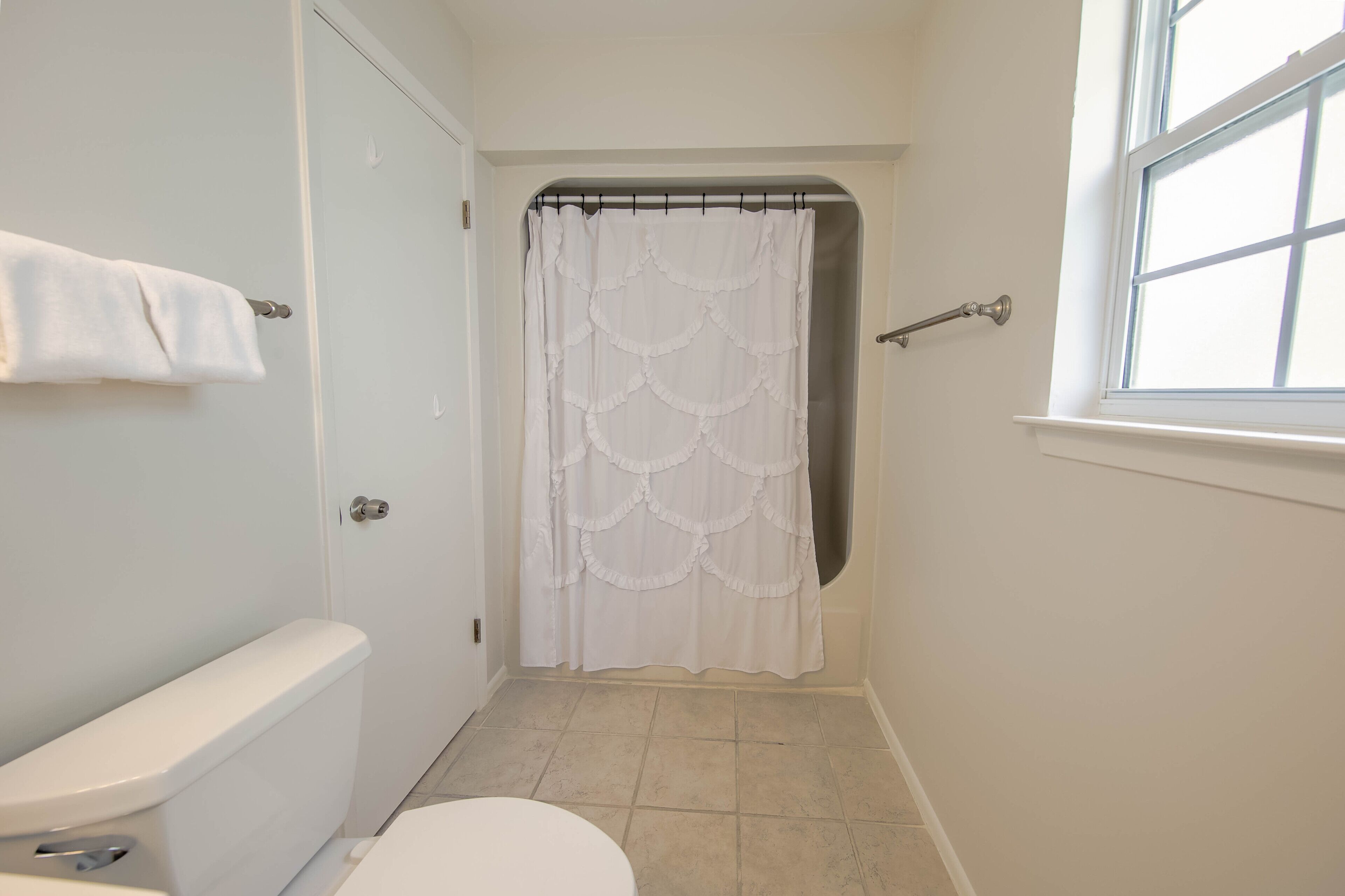 Un bany amb vàter, un lavabo, cortina de bany i una finestra.