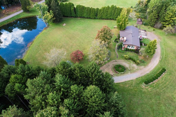 An aerial view of a residential property with a pond, a well-maintained lawn, and a house with a sloped roof.