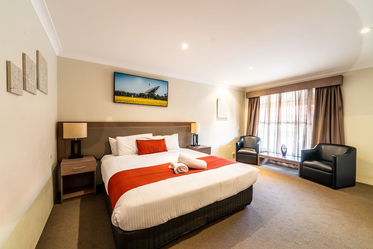 A hotel room with a large bed, a desk, a chair, and a window with curtains.