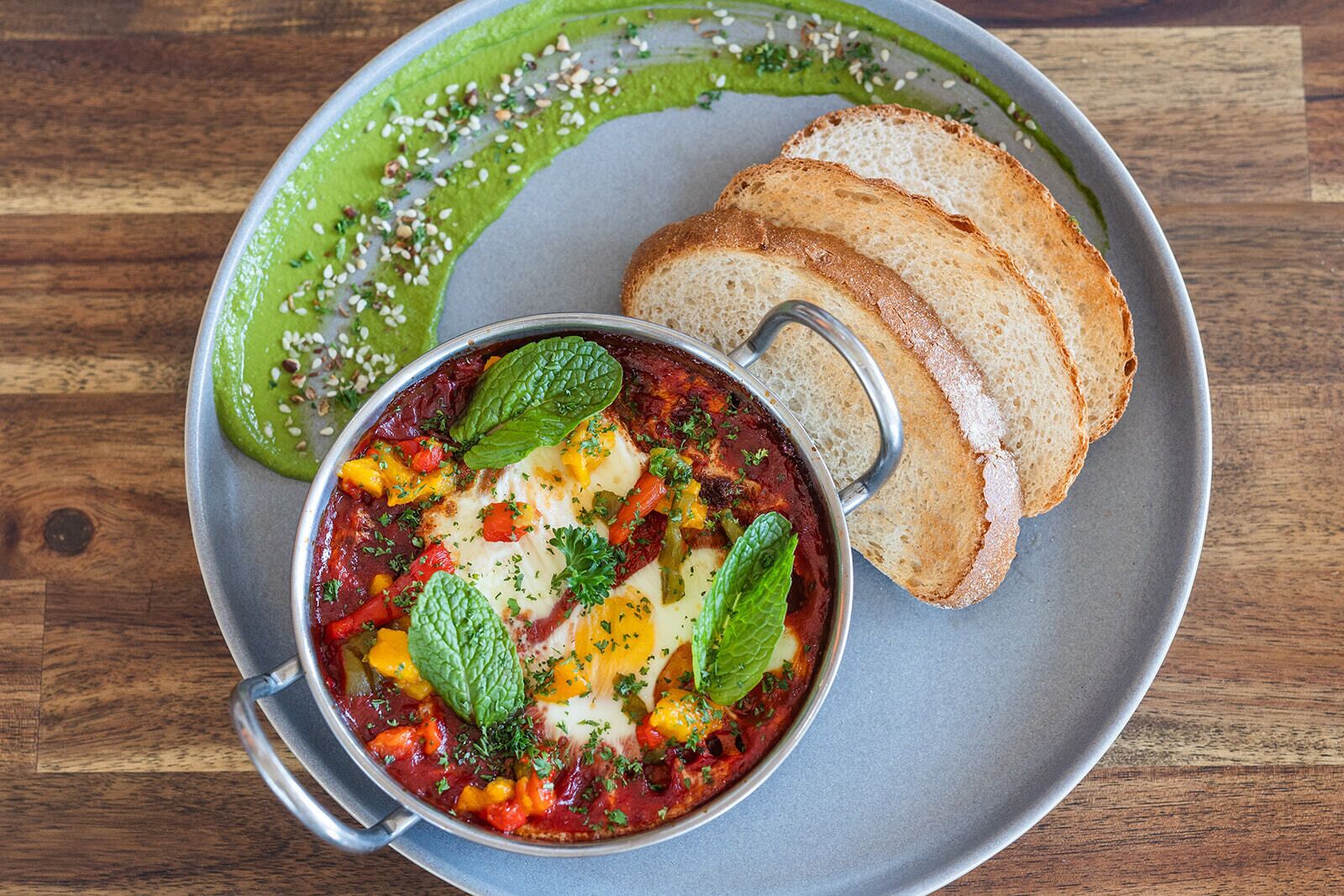 A bowl of shakshuka with bread on a plate.
