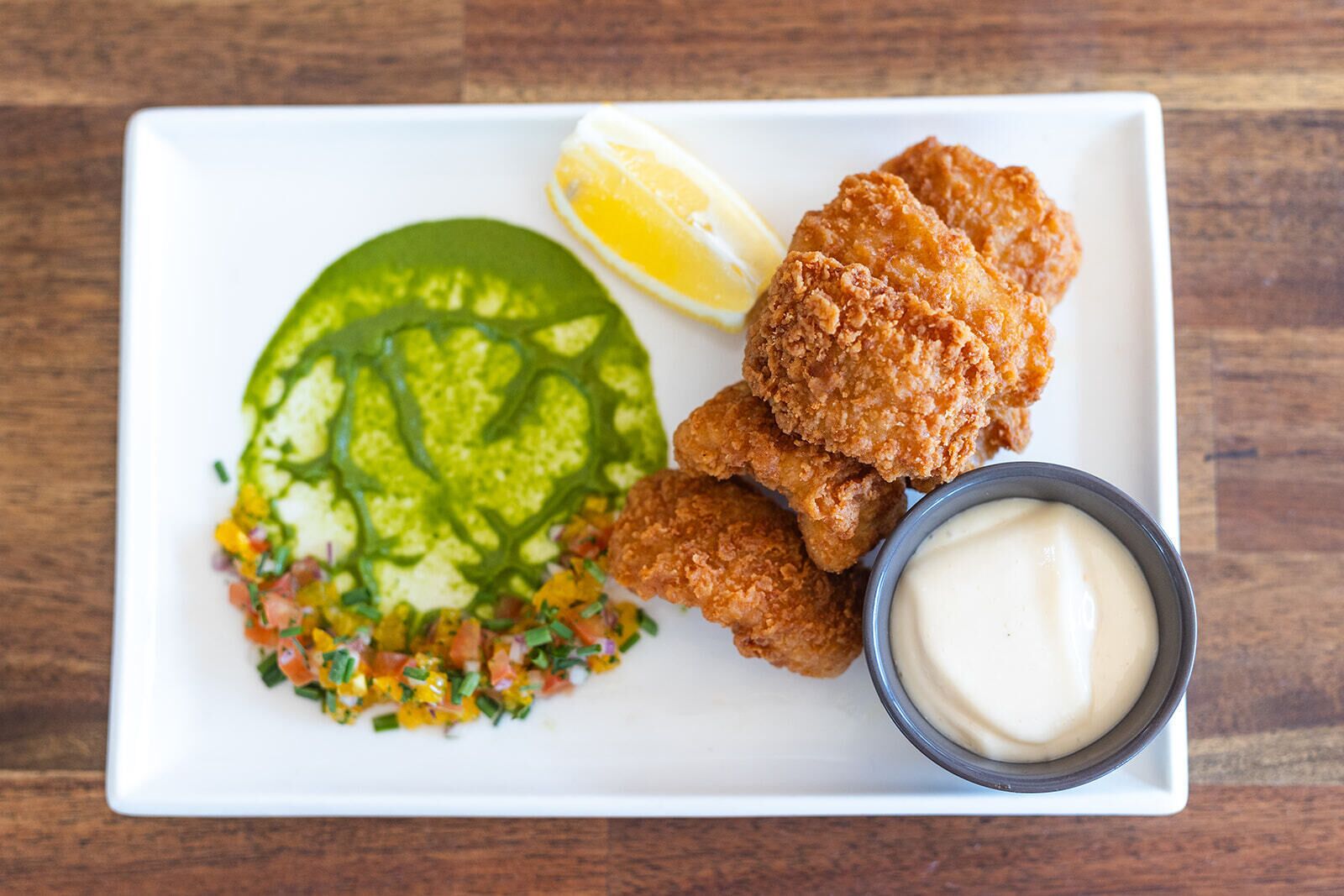 A plate with fried chicken, a slice of lemon, a green salad, and a small bowl of sauce.