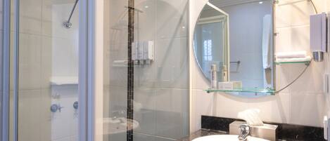 Un baño moderno con ducha envuelta en vidrio, espejo redondo y lavamanos blanco.