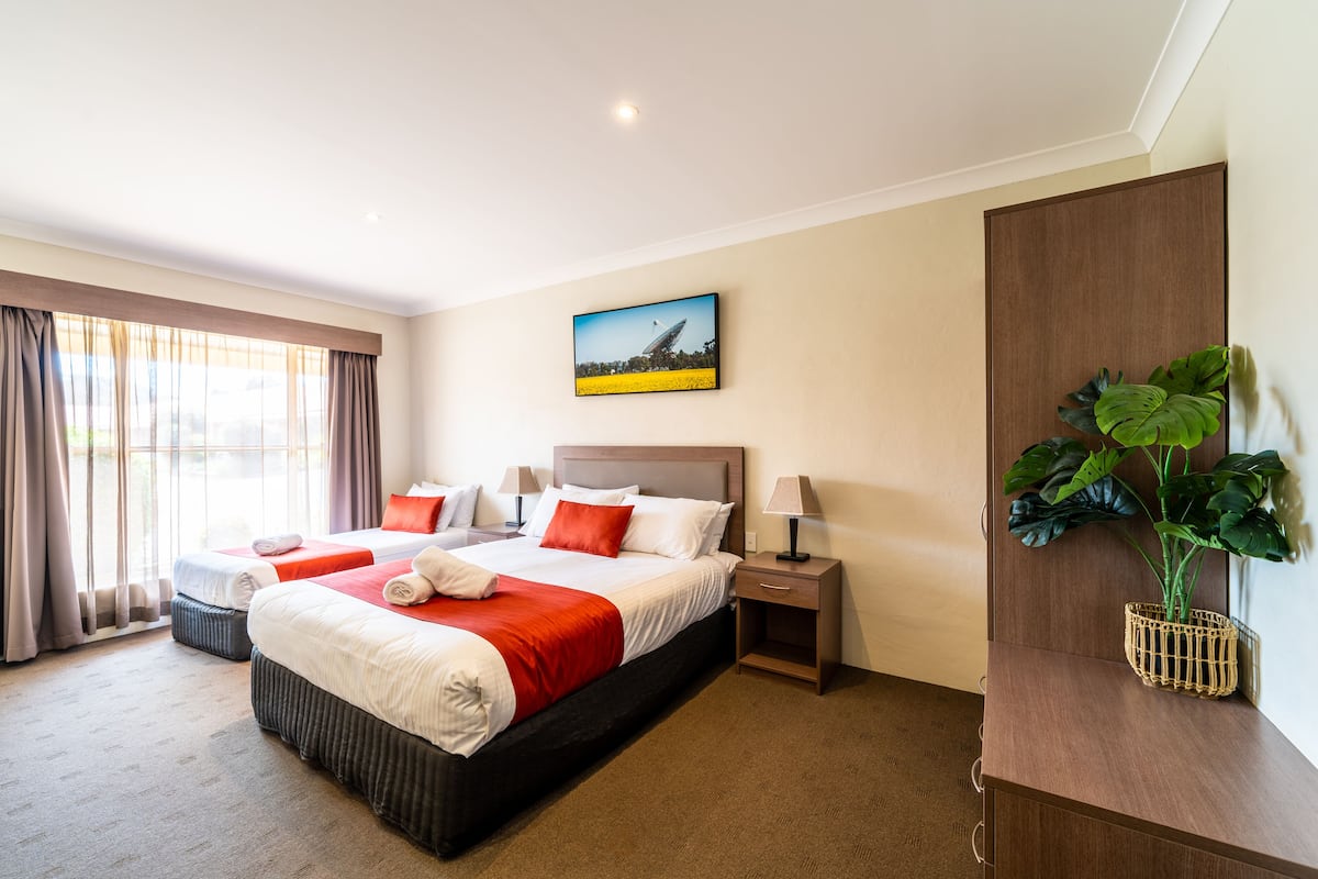 A hotel room with a large bed, two bedside tables, a nightstand, a potted plant, and a painting on the wall.