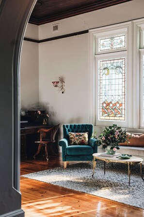 Ein Zimmer mit Holzboden, einem blaugrünen Sessel, einem weißen Couchtisch und einem Buntglasfenster.