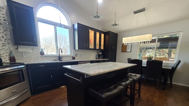 Una cocina moderna con armarios oscuros, una isla grande con taburetes de bar, horno empotrado y ventana que proporciona luz natural.