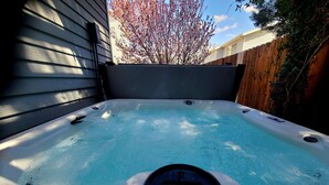 Un jacuzzi con asiento integrado, rodeado por una valla de madera y un árbol con flores rosadas.