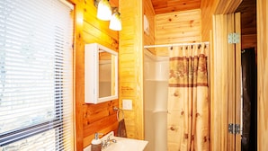 A wooden cabin bathroom with a white sink, a mirror, and a shower curtain. - Bigfoot Lodge Room One (Benton)