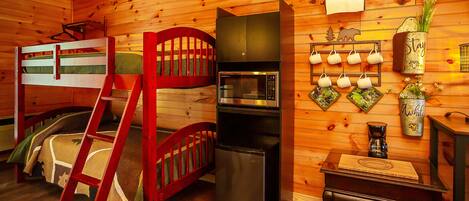 A cozy cabin interior with a bunk bed, a refrigerator, a microwave, and a wall-mounted coffee maker.