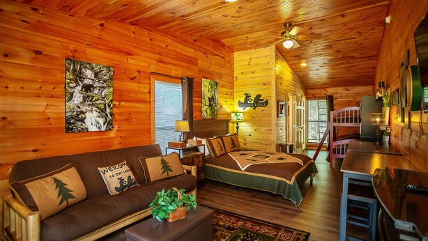 A cozy cabin interior with a wooden interior, a sofa, a bed, and a dining area. - Bigfoot Lodge Room One (Benton)