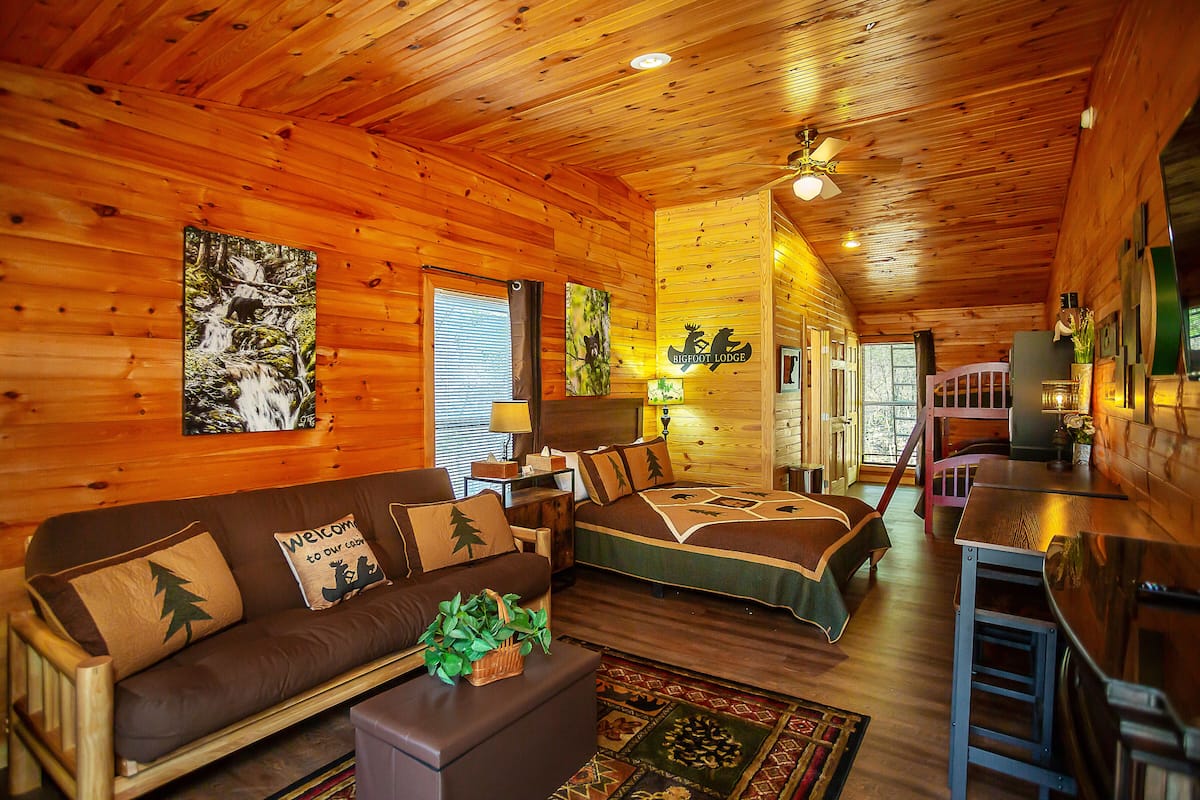A cozy cabin interior with a wooden interior, a sofa, a bed, and a dining area.