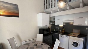 Uma cozinha compacta com armários brancos, máquina de lavar embutida e área de refeições com mesa e cadeiras redondas.