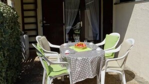 Um pátio com mesa e cadeiras, um pequeno jardim e um edifício com telhado de telhas.