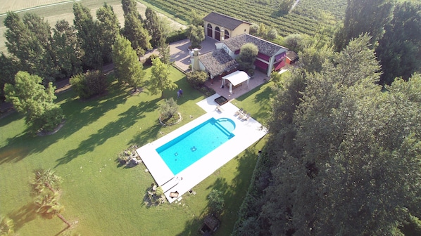 Eine Vogelperspektive auf ein Anwesen mit Swimmingpool, einem großen Haus mit Ziegeldach und umliegender Bepflanzung.