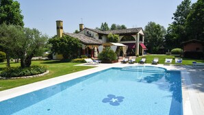 Una piscina con sillas de descanso, una casa con techo de tejas y un jardín bien cuidado.
