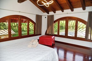 Ein Schlafzimmer mit einem großen Bett, einer roten Bank und hohen, bogenförmigen Fenstern mit Vorhängen.