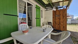 Un pequeño espacio exterior con comedor, una mesa y sillas blancas, una puerta verde y una valla de madera.