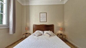 Un dormitorio con una cama grande, dos mesitas de noche con lámparas, una ventana con cortinas y una obra de arte enmarcada en la pared.