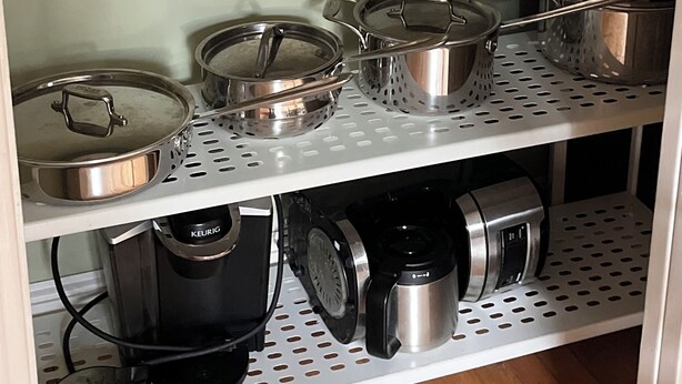 Una cocina con un horno tostador en el estante superior, varias ollas y sartenes en el estante central y una cafetera en el estante inferior.