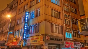 Um hotel com vários andares, um letreiro chamativo com a inscrição 'HOTEL CAMILA', várias janelas e uma entrada visível.