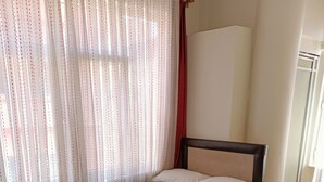 Quarto de hotel com duas camas, uma janela grande com cortinas leves e piso de madeira.