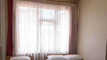 Une chambre avec deux lits simples, un ventilateur de plafond et des rideaux légers.