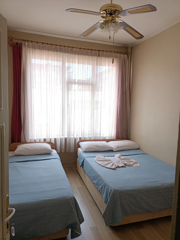 Una habitación con dos camas individuales, un ventilador de techo y cortinas translúcidas.