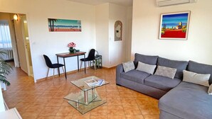Ein Wohnzimmer mit grauem Sofa, einem Glastisch und einem Essbereich mit Tisch und Stühlen.