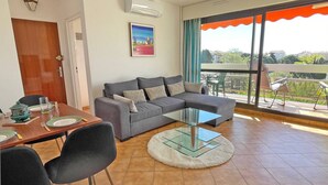 Ein modernes Wohnzimmer mit einem grauen Sofa, einem Glastisch und einem Essbereich mit einem Holztisch, gedeckt für zwei Personen.