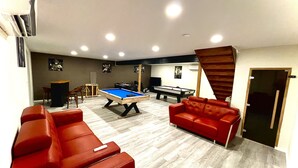 Una habitación con mesa de billar, sofás de cuero rojo, mesa de snooker y una escalera.